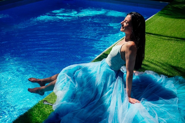 Mulher indiana posando em vestido longo azul perto da piscina