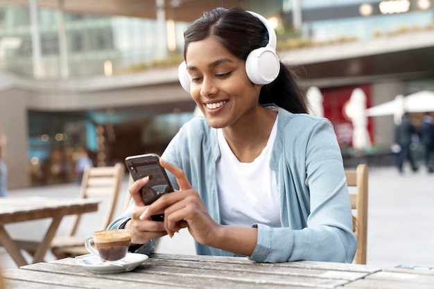 Foto mulher indiana sorridente segurando o celular fazendo compras on-line, lendo mensagem de texto sentada no café