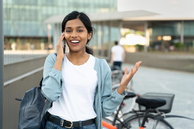 Mulher indiana sorridente vestindo roupas casuais falando no celular olhando para a câmera ao ar livre