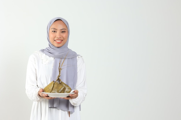 Mulher indonésia segurando prato branco com bolo de arroz em forma de diamante para festa muçulmana