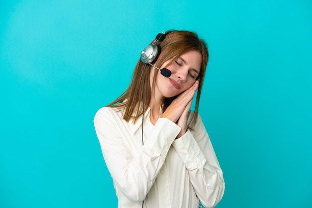 Mulher inglesa de telemarketing trabalhando com um fone de ouvido isolado em fundo azul, fazendo gesto de sono em expressão adorável