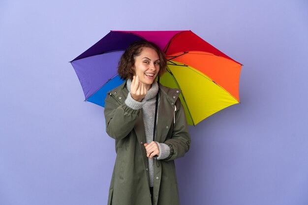 Mulher inglesa segurando um guarda-chuva sobre fundo roxo fazendo gesto de dinheiro