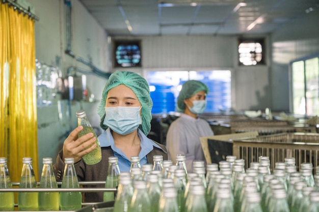 Mulher inspetora verificando uma bebida de frutas engarrafada na linha de produção do transportador na fábrica de bebidas de processamento