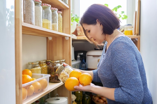 Mulher interior de cozinha despensa em casa segurando laranjas no armazenamento de alimentos de mãos