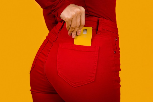 Mulher irreconhecível colocando cartão de crédito amarelo no bolso da calça vermelha