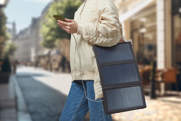 Mulher irreconhecível com bateria solar flexível segurando smartphone no fundo de uma cidade