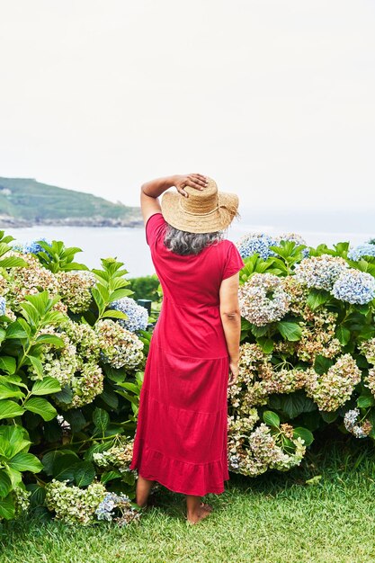 Mulher irreconhecível de meia-idade com vestido vermelho olhando o mar