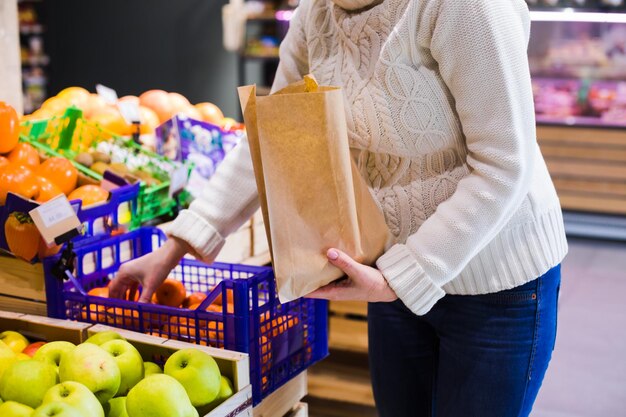 Mulher irreconhecível escolhe e compra produtos colocando-os em saco de papel frutas e legumes frescos na loja local eco shopping no comércio local