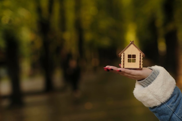 Mulher irreconhecível segurando pequena casa de madeira no parque florestal Parte do corpo da mulher com casa de brinquedo Conceito de compra de telhado de apartamento novo em local ecológico