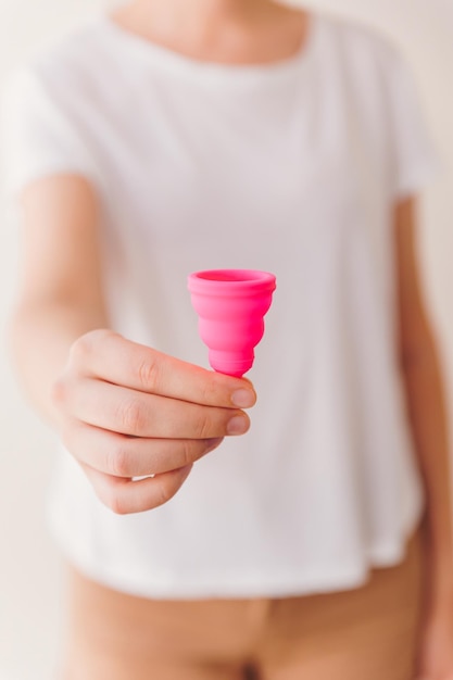 Mulher irreconhecível segurando um copo menstrual rosa close-up Período e conceito de higiene feminina