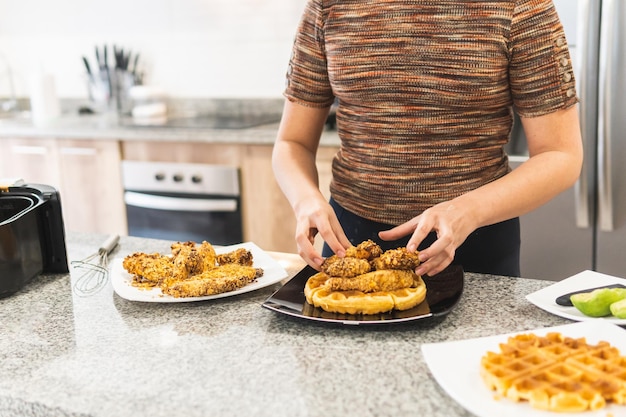 Mulher irreconhecível servindo frango frito empanado com cereais sobre waffles e calda