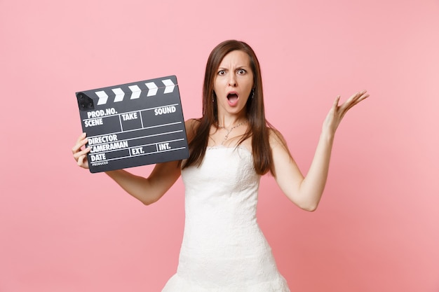 Mulher irritada em vestido branco xingando espalhando a mão segurando um clássico filme preto fazendo claquete