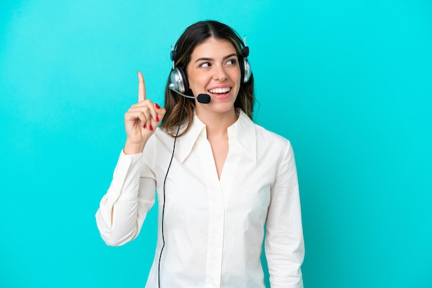 Mulher italiana de telemarketing trabalhando com um fone de ouvido isolado em fundo azul com a intenção de realizar a solução enquanto levanta um dedo