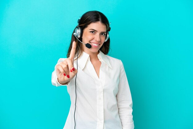 Mulher italiana de telemarketing trabalhando com um fone de ouvido isolado em fundo azul mostrando e levantando um dedo
