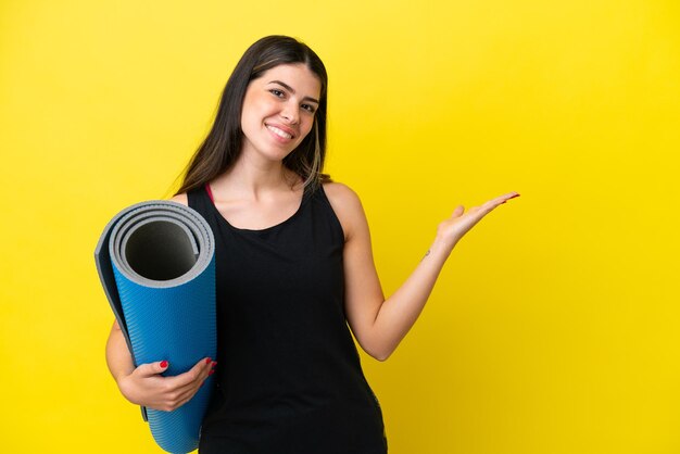 Mulher italiana esportiva indo para aulas de ioga isoladas em fundo amarelo, estendendo as mãos para o lado para convidar para vir