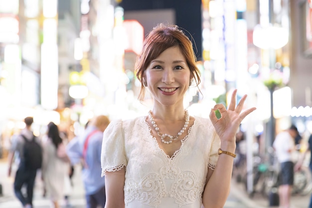 Mulher japonesa com vestido branco glamouroso nas ruas de Tóquio, Japão. Ok gesto