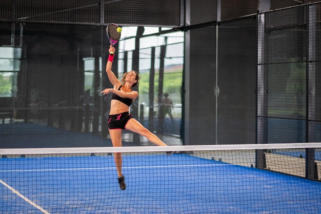 Foto mulher jogando pádel em uma quadra de pádel de grama azul - jovem jogadora de pádel esportiva batendo na bola