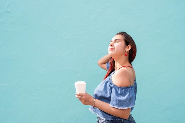Foto mulher jovem a beber café a desfrutar do sol contra um fundo azul