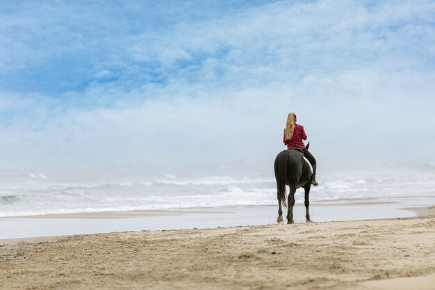 Mulher jovem a cavalo na praia em um dia nublado