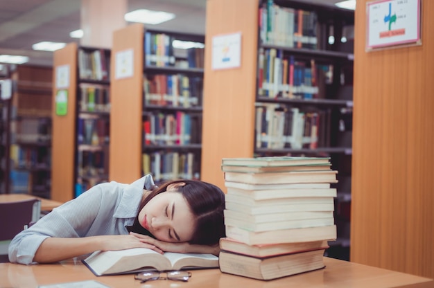 Mulher jovem a dormir à mesa na biblioteca.