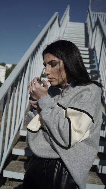 Foto mulher jovem a fumar em frente à escada.