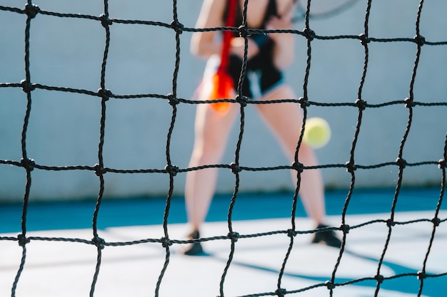 Foto mulher jovem a jogar ténis do outro lado da rede de ténis