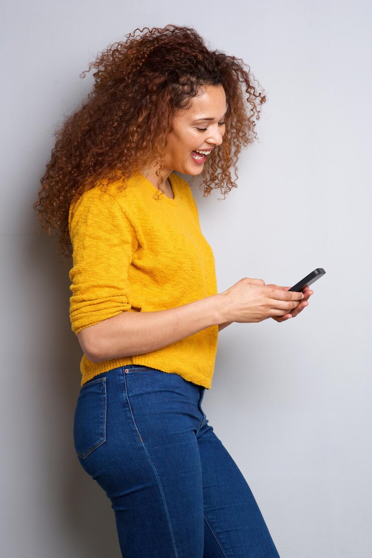 Mulher jovem a olhar para o telemóvel e a rir.