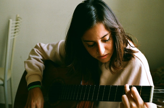 Foto mulher jovem a tocar guitarra em casa.
