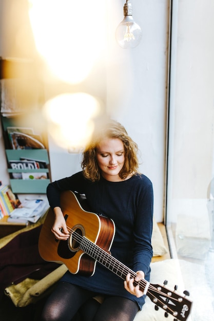 Foto mulher jovem a tocar guitarra em casa.