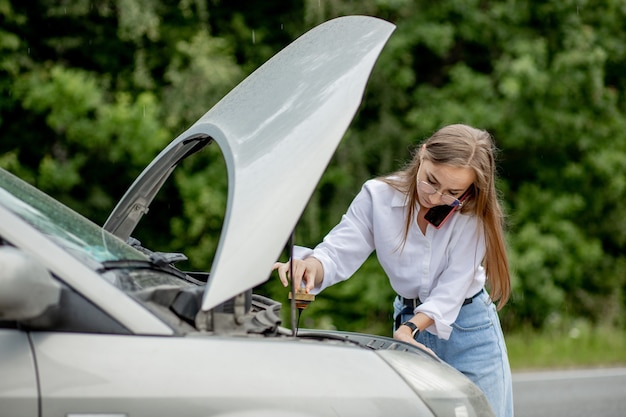 Foto mulher jovem abrindo o capô de um carro quebrado, tendo problemas com o veículo