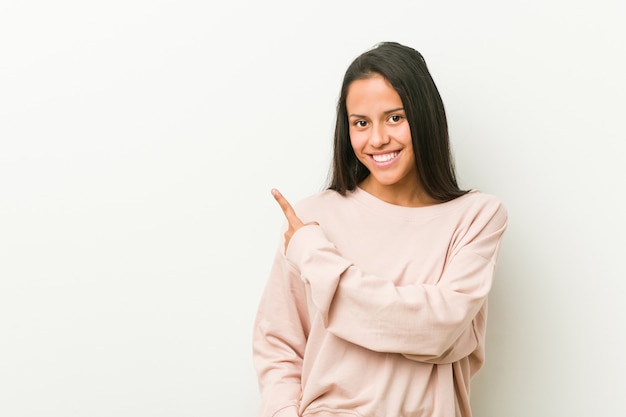 Mulher jovem adolescente bonito hispânico sorrindo e apontando de lado, mostrando algo no espaço em branco.