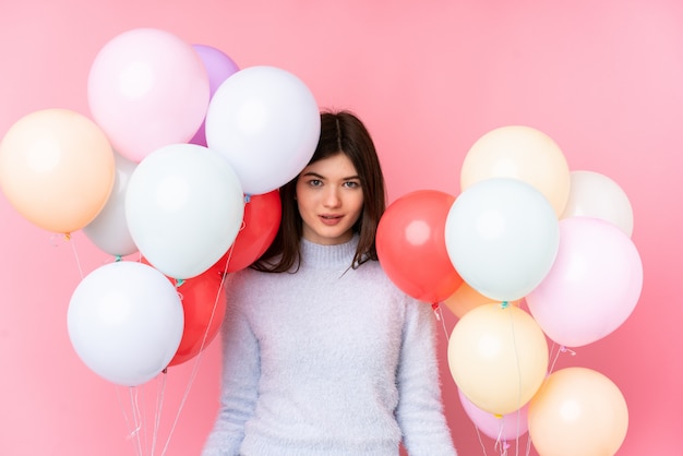 Mulher jovem adolescente ucraniano segurando muitos balões sobre parede rosa isolada