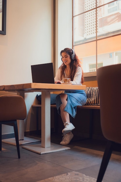 Mulher jovem adulta trabalha em um laptop de um restaurante enquanto ouve música