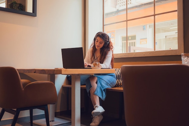 Mulher jovem adulta trabalha em um laptop de um restaurante enquanto ouve música