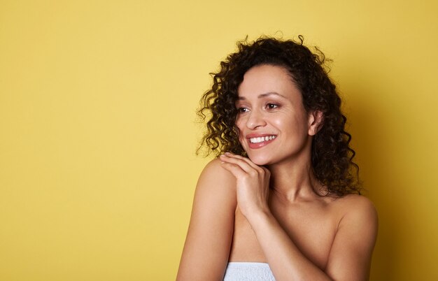 Foto mulher jovem afro-americana atraente com cabelo encaracolado, olhando para longe e sorrindo com um sorriso cheio de dentes. copie o espaço