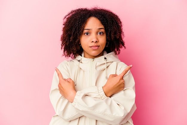 Mulher jovem afro-americana de raça mista isolada pontos lateralmente, está tentando escolher entre duas opções.