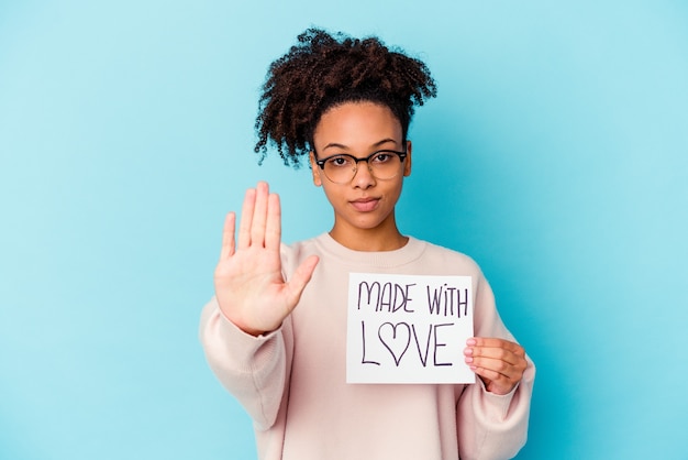 Mulher jovem afro-americana de raça mista segurando um conceito feito com amor em pé com a mão estendida, mostrando o sinal de stop, impedindo-o.
