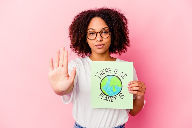 Mulher jovem afro-americana de raça mista segurando um papelão de conceito de proteção mundial em pé com a mão estendida, mostrando o sinal de stop, impedindo-o.