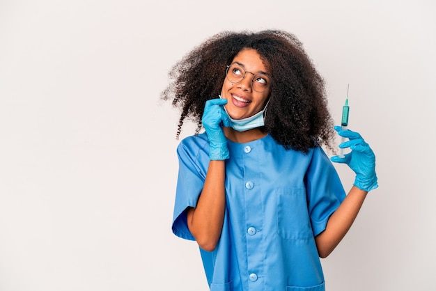 Mulher jovem afro-americano encaracolado médico segurando uma seringa relaxada pensando em algo olhando para um espaço de cópia.