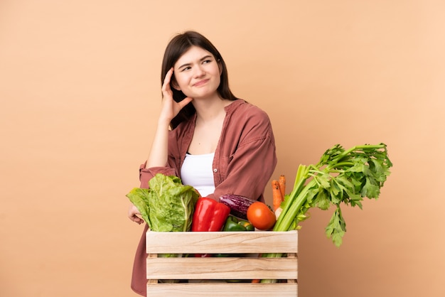 Mulher jovem agricultor com legumes recém colhidos em uma caixa com dúvidas