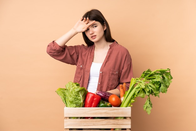 Mulher jovem agricultor com legumes recém colhidos em uma caixa com expressão cansada e doente