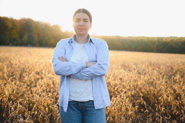 Mulher jovem agricultora parada no campo de soja no verão segurando tablet e monitorando o crescimento das culturas