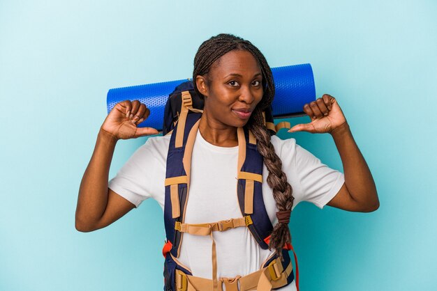 Mulher jovem alpinista afro-americana isolada sobre fundo azul sente-se orgulhosa e autoconfiante, exemplo a seguir.