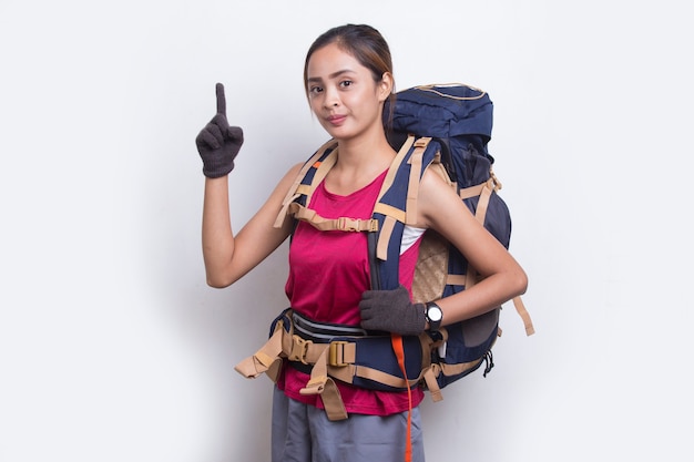 Mulher jovem alpinista asiática com mochila apontando o dedo no espaço vazio no fundo branco