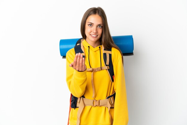 Mulher jovem alpinista com uma mochila grande sobre fundo branco isolado, convidando a vir com a mão. Feliz que você veio