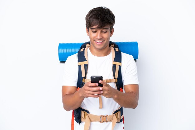 Mulher jovem alpinista com uma mochila grande sobre fundo branco isolado, enviando uma mensagem com o celular