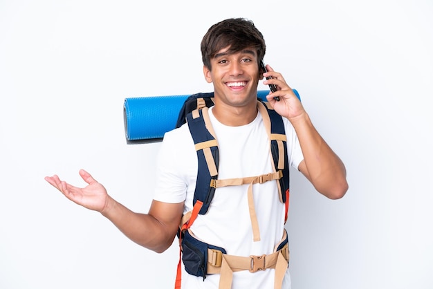 Mulher jovem alpinista com uma mochila grande sobre fundo branco isolado, mantendo uma conversa com o celular com alguém