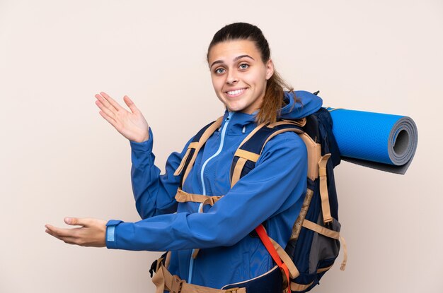 Mulher jovem alpinista com uma mochila grande sobre parede isolada, estendendo as mãos para o lado para convidar para vir