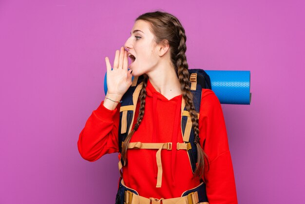 Mulher jovem alpinista com uma mochila grande sobre parede isolada