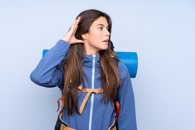 Mulher jovem alpinista com uma mochila grande sobre parede isolada